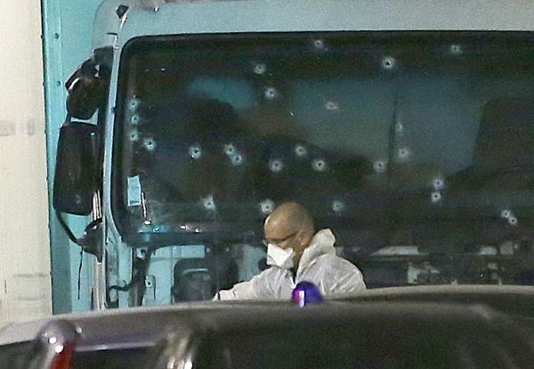A forensic officer stands near a van with its windscreen riddled with bullets