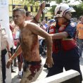 Záchranář odvádí zraněného muže během vzpoury ve městě Barquisimeto.