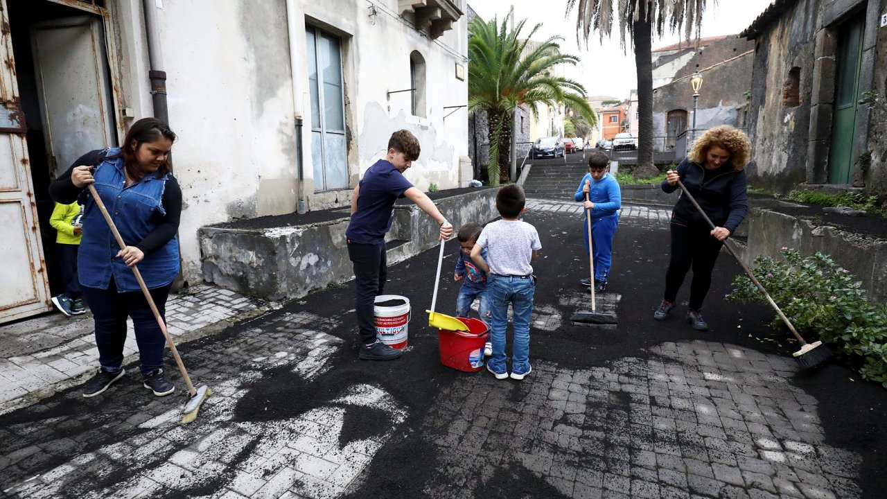 Lidé čistící ulici pokrytou sopečným popelem z Etny v Piedimonte Etneo.