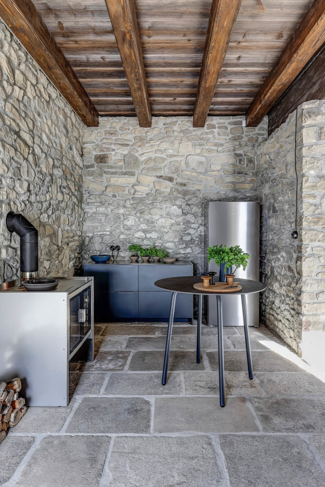 Jestli má dům Mezi lukami nějaké poznávací znamení, je to lustr od italského designéra Davida Groppiho. Modřínová okna mezitím pouští do prostoru světlo, jedlové trámy lákají k úkrytu a v kuchyni na vás pomrkávají moderní kamna od britských Firebelly Stoves, hned vedle skříněk dánského výrobce Reform. Tady chcete snít, třeba na venkovní posteli s výhledem na nekonečně zelené kopce.
