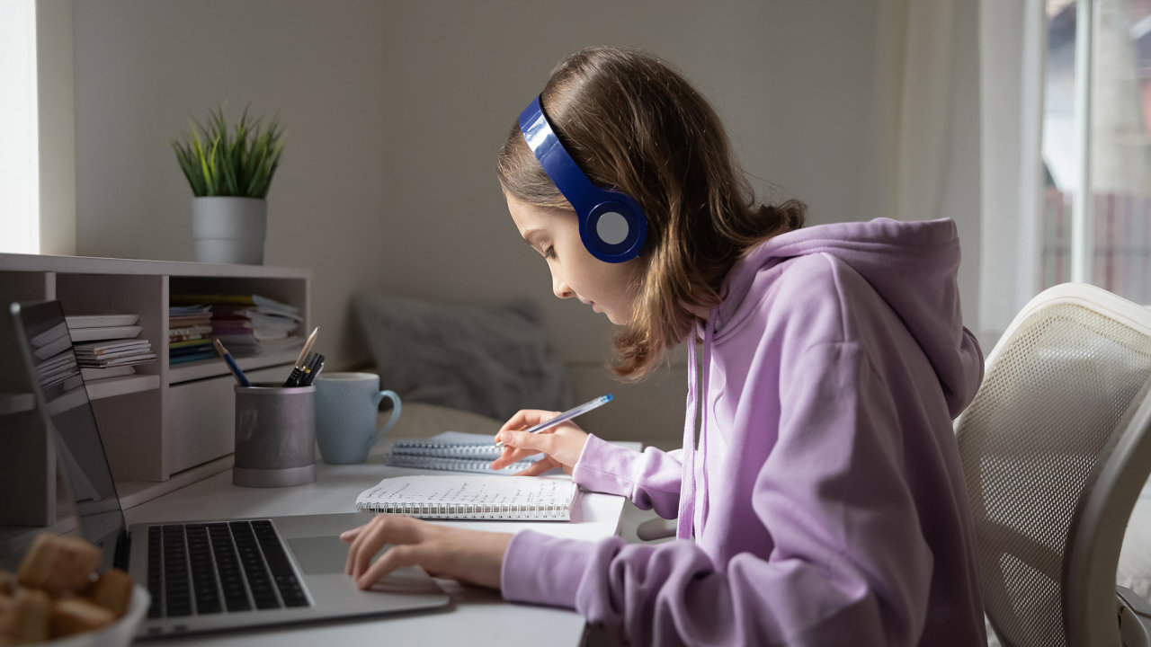 Teen girl school pupil wearing headphones studying online from home making notes. Teenage student distance learning on laptop doing homework