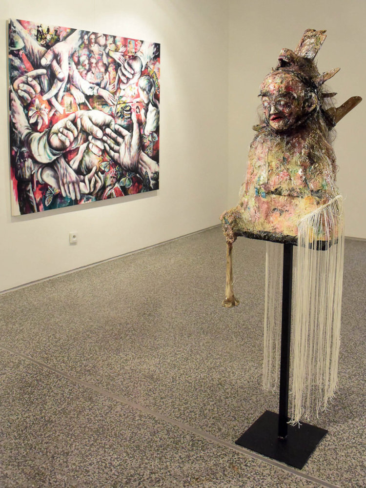 Existenz, polyuretan, silikon, dřevo z Pacifiku, umělá kost a další materiály, 170 × 50 cm. V pozadí ghost fingers, kombinovaná technika, malba na plátně, 180 × 150 cm